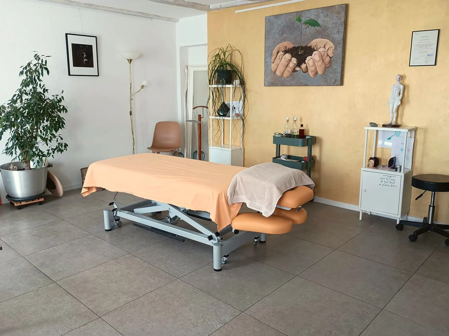 Le cabinet d’Aurélie à Coffrane : table de massage, mur doré, plantes et son brevet fédéral encadré