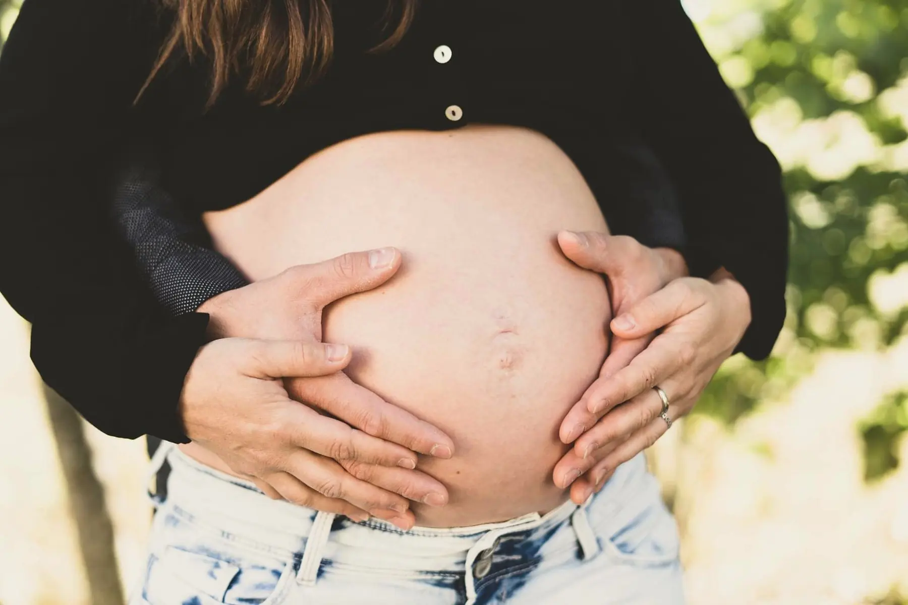 Ventre arrondi d’une femme enceinte, des mains posées dessus avec douceur