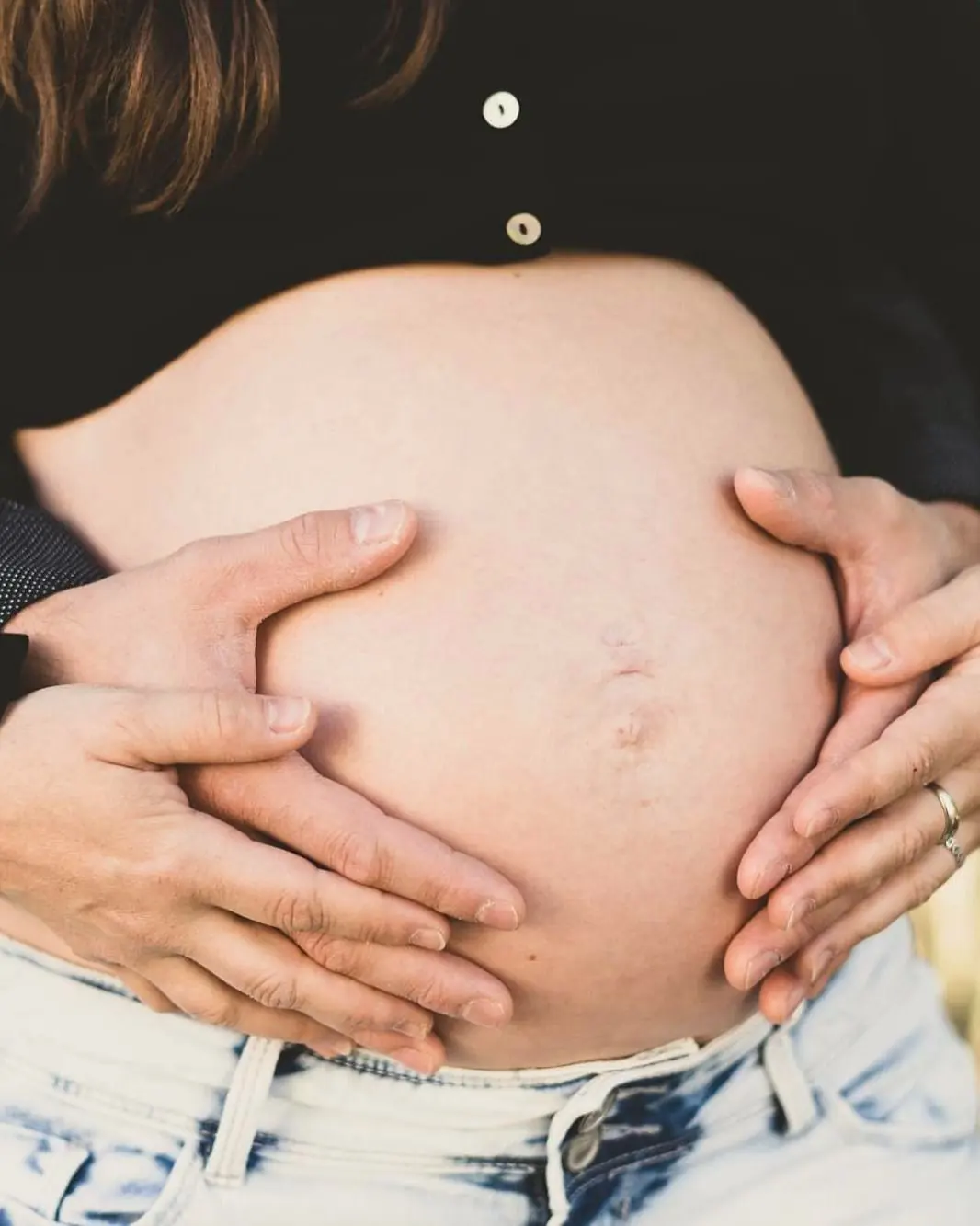 Ventre arrondi d’une femme enceinte, des mains posées dessus