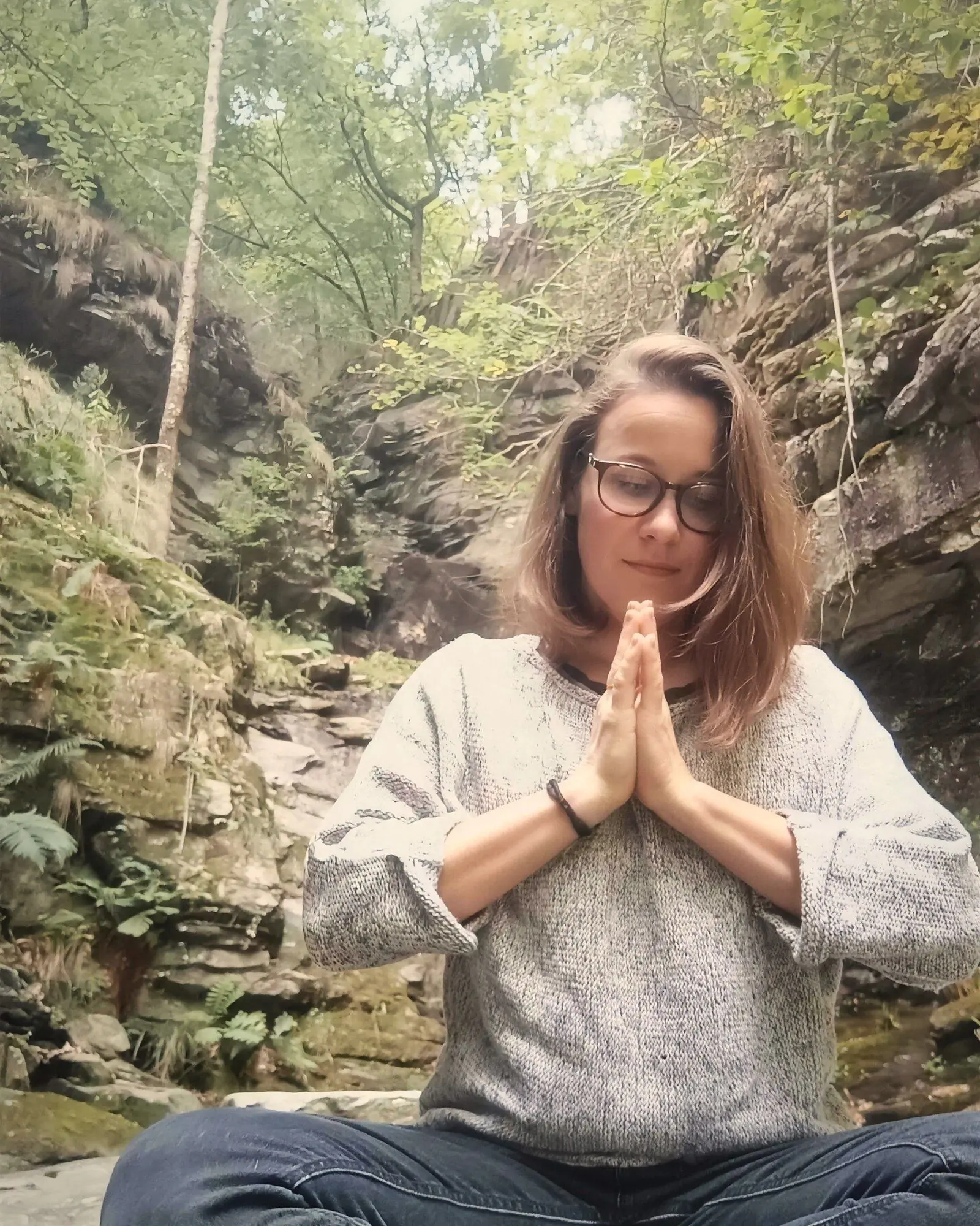 Aurélie Gamboni en méditation, les mains jointes, dans une gorge boisée