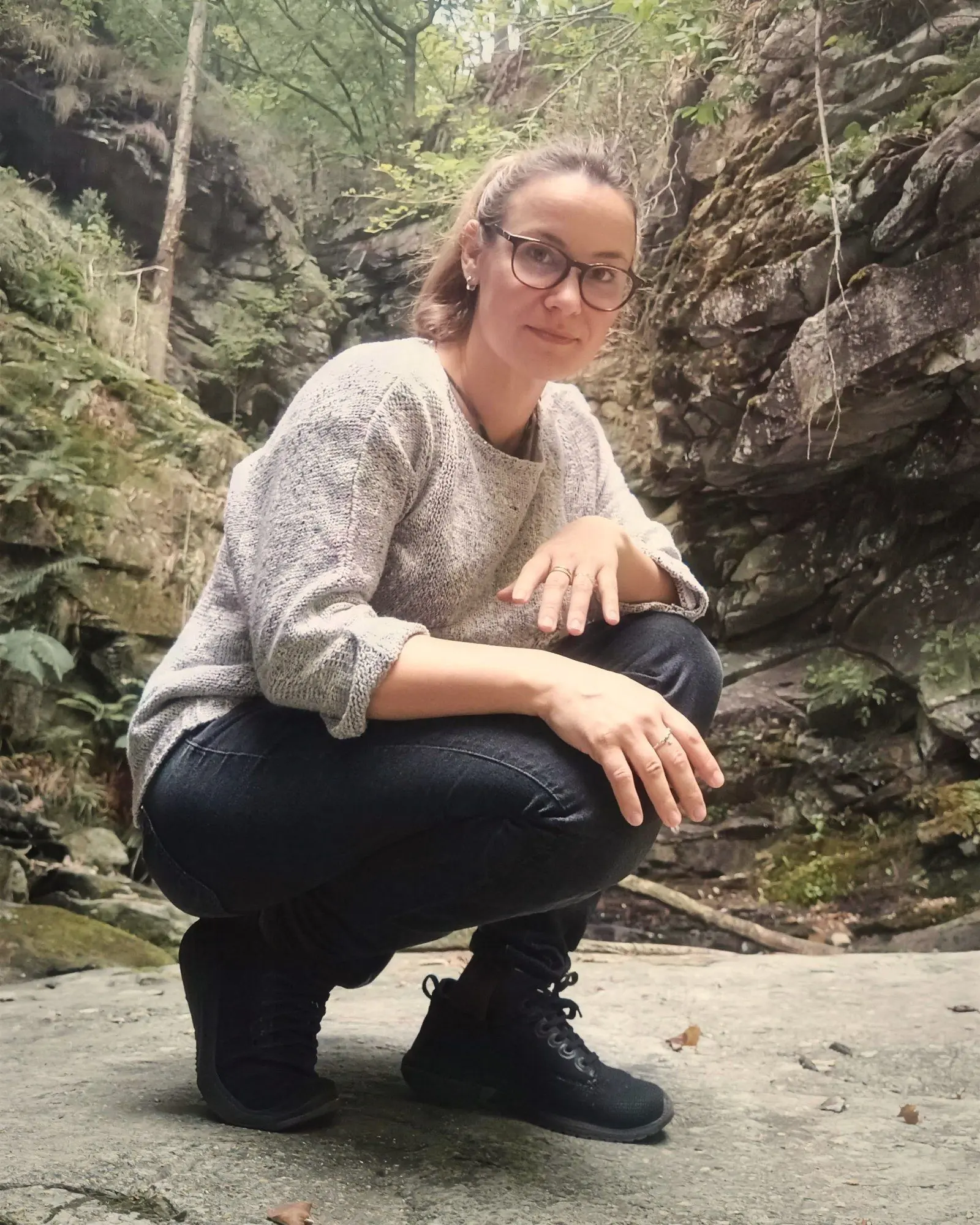 Aurélie Gamboni, accroupie sur un rocher dans une gorge boisée, souriante